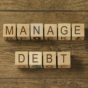 Wooden blocks spell 'MANAGE' and 'DEBT' on a surface, symbolizing effective handling of financial obligations